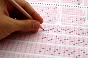 Mão segurando gabarito do Enem e conferindo respostas da prova para calcular a nota